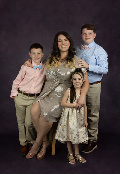 mom-with-3-children-wearing-gold-sparkly-dress-and-pinks-and-blues-in-studio-arlington-tx-against-purple-backdrop