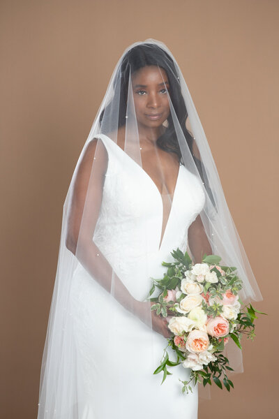 Bride wearing a cathedral length veil with blusher and pearls, and holding a white and blush bouquet