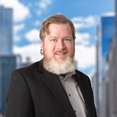 Headshot photo of a man in a suit with a blue sky background.