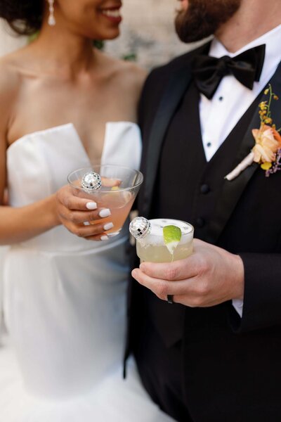 bride and groom smile at each other while holding cocktails with disco ball stirrers