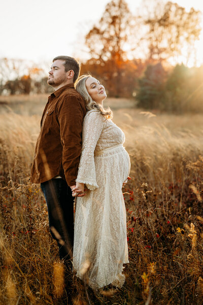 Couple stands back to back while the mother holds her pregnant belly.