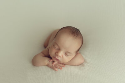 A newborn baby sleeps with its head on its hands on a green blanket