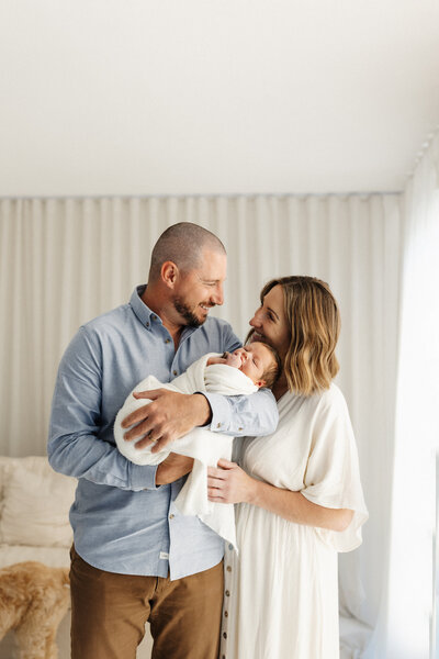 a mother and father wearing their favourite clothes holding their newborn baby during their photoshoot with lucy jane photography in christchurch