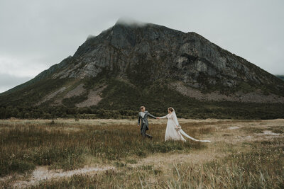 Wedding couple walking in a field in front of a high mountain in Senja norway