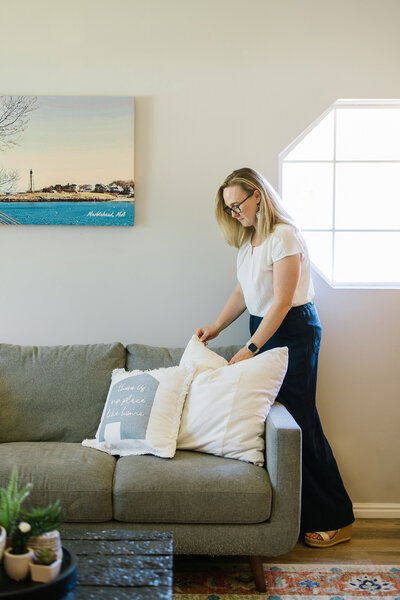 Kim Kussman, Utah Realtor & Owner of Nurture Lane, arranging pillows in the living room of a realty listing