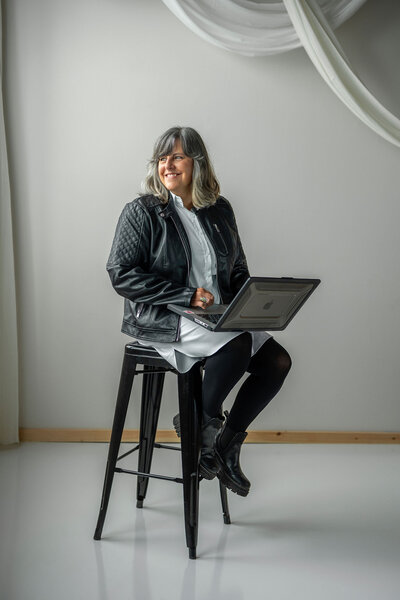 Jocelyn sitting on a stool with a laptop looking to the side