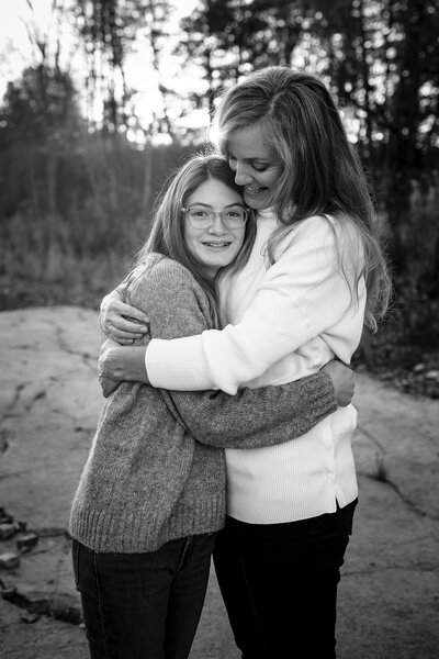 Black-and-white portrait of a mother and daughter embracing with smiles, set against a nature backdrop at a local Kingston park.