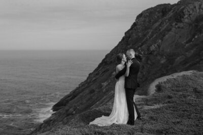 bride and groom embrace beside a dramatic sea cliff
