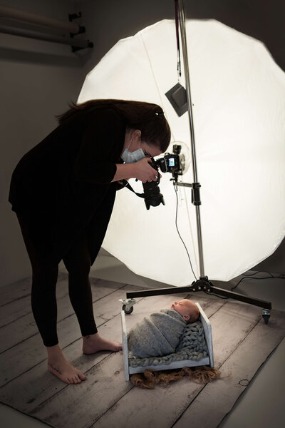 Newborn Photographer taking a photo of a swaddled newborn  baby in a small bed