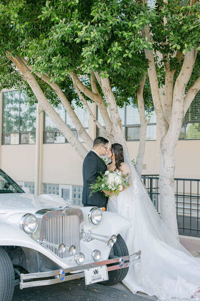 Elegant wedding session by a vintage car: The bride and groom stand close, gazing lovingly into each other's eyes, capturing a moment of timeless romance
