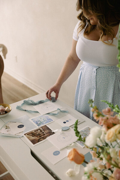 Wedding planner, Zelie & Co., creating a blue wedding invitation suite flat lay next to a flower bouquet