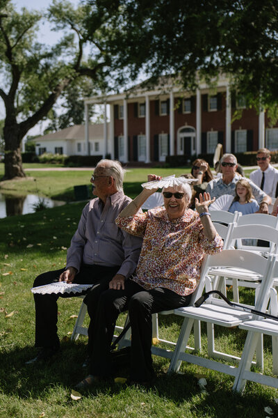 Two wedding guests sitting waiting for the ceremony to start with their fans.