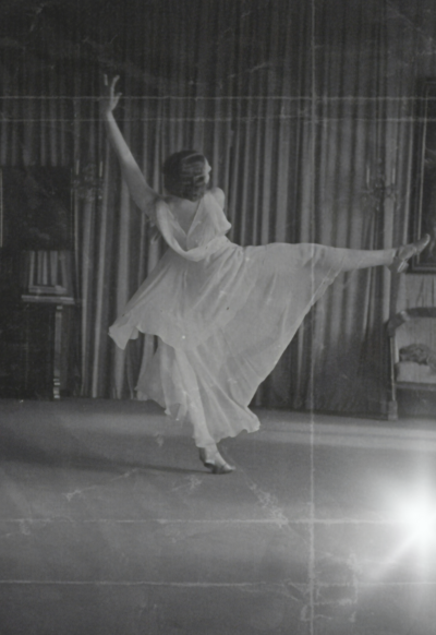Black and white filtered film photo of a 1920's woman dancing elegantly in a flowy, white dress.