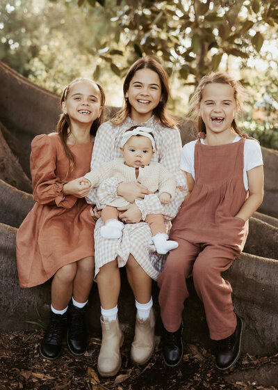 Three big sisters with their little baby sister smiling for family photoshoot in Sydney