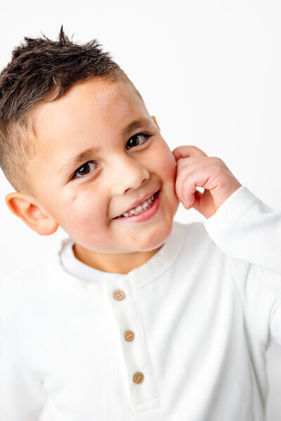 Boy smiles at camera in a white studio.