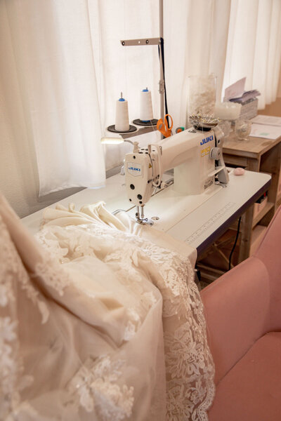 A lace wedding dress laid across a sewing machine, ready for alterations