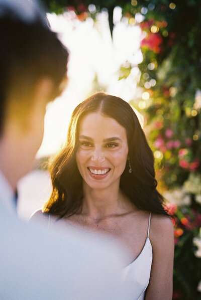 Bride smiling tenderly at her groom during the ceremony, surrounded by golden sunlight and floral details — emotional wedding moment captured by Asia Pimentel Photography.