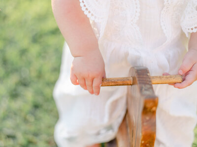 One year old girl holding onto rocking horse.