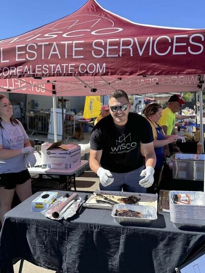 person in black Wisco T-Shirt serving brisket under red popup shelter