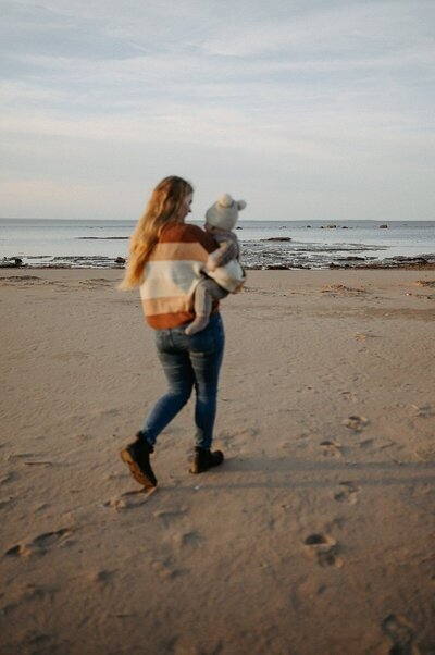 Liten tjej kramar om sin mamma i famnen på stranden.