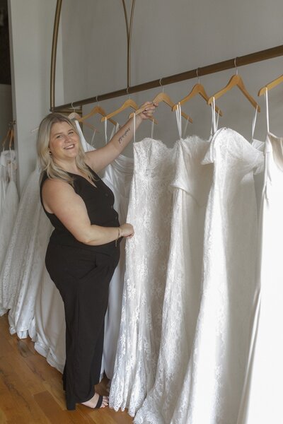 Woman holding a wedding dress on a hanger, smiling at the camera.