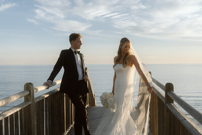 Bride and groom stand on boardwalk at sunset