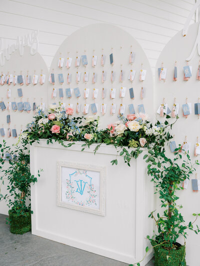 wedding details of seating chart with three white arches and individual ribbon tags and overflowing florals