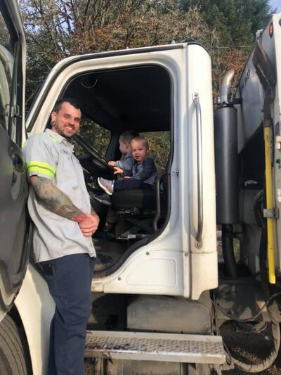 Steve and a child smile from the cab of a Ecosystems garbage truck.