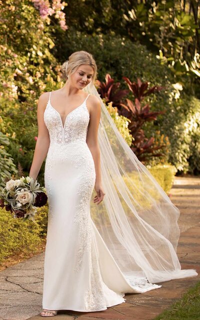 SEXY SHEATH WEDDING DRESS WITH SHAPED TRAIN Talk about a smooth, sultry statement! Let your natural beauty shine in this stunner from Essense of Australia. The perfect combination of sheer lace detail and soft, clean crepe, you’ll feel as good as you look in this relaxed silhouette. A clean-cut, V-neckline and shoestring straps frame your neck and shoulders beautifully, as the semi-sheer bodice is crafted with gorgeous floral appliqués and a layer of glitter tulle for a subtle shine. the laces extend over the waistline and elongate over the sides of the hips to sculpt the body, while visible seaming on the skirt adds some structure to the very slight fit-and-flare feel. The low, open back is framed with sheer panels and floating linear designs along the base for a touch of extra detail, as fabric-covered buttons continue throughout the silhouette and down to the edge of the gently scalloped train with a lace finish.