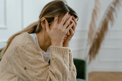 A distressed woman sitting with her head in her hands, representing anxiety and overwhelm—Emily Austin Therapy can help.