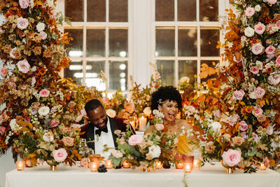 Lush growing florals surround the couple at this autumnal wedding’s sweetheart table composed of roses, ranunculus, lisianthus, dried hydrangea, delphinium, copper beech, and fall foliage creating hues of dusty rose, burgundy, mauve, copper, terra cotta, and hints of lavender. Design by Rosemary and Finch in Nashville, TN.
