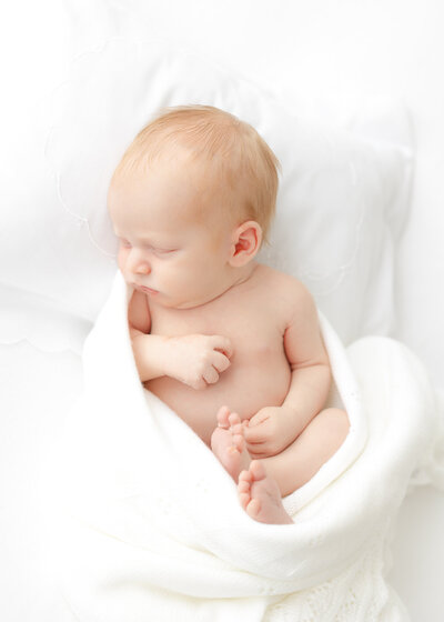 Young mom wearing a pink dress from CCP's client closet holding her newborn baby boy wrapped in a white and blue bow swaddle. She is looking at him with eyes full of love