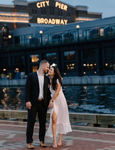 beautiful engaged couple holding hands at fells point pier boardwalk nighttime in baltimore maryland