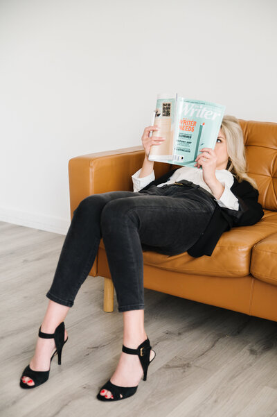 Sarah Klongerbo laying back on a leather couch in black jeans and heels reading a magazine