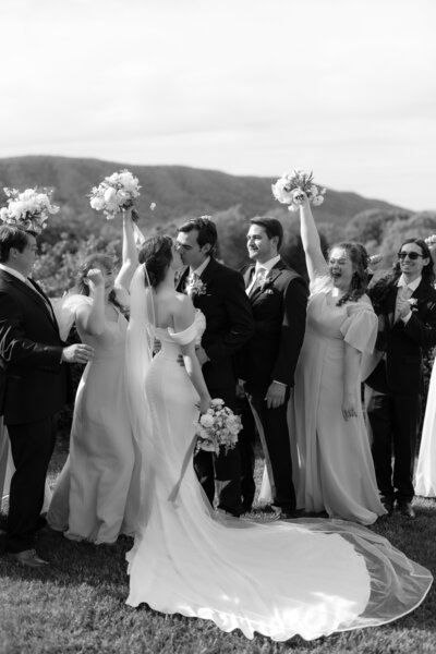 newlywed couple kissing while their wedding party celebrates them