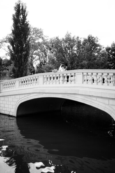 Bride with veil holding onto her groom on a bridge with water in Forest Park, STL