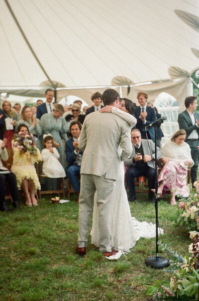 Newlyweds dance together in the grass while their attendees watch in the distance