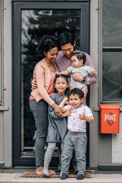 A family with three young children stand on their front porch during a lifestyle family photography session by Kate Simpson Photography in Minneapolis.
