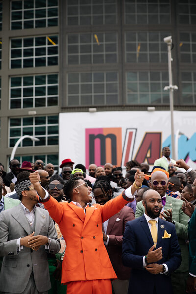 A large group photo of black men wearing suits cheering together