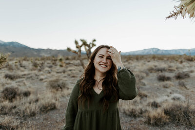Katelyn reaches up and removes a piece of hair from her face while smiling in the desert.