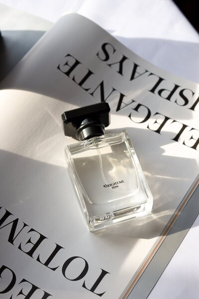 A close up of a perfume bottle lying ontop of an open fashion magazine with large serif typography.