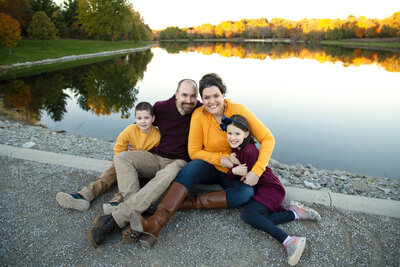 Family of four snuggling together in front of lake at Kent Park. 