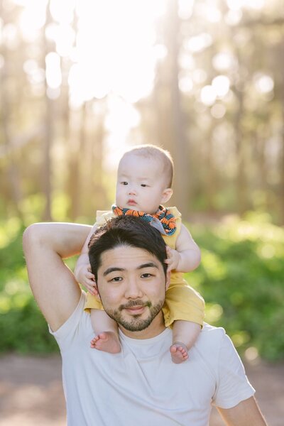 A man holds a baby on his shoulders, smiling.