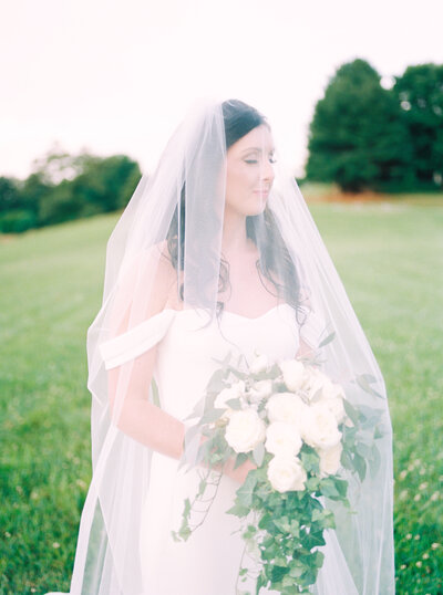 Bride with veil over her face while holding white bouquet with eyes closed