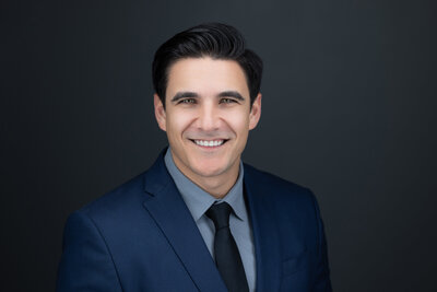 A clear crisp headshot of a Sacramento attorney looking straight at the camera in a blue suit and a grey backdrop. Photo taken at Sacramento photography studio, philippe studio pro.