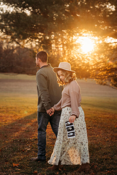 Couple walk hand in hand while holding their sonogram photo. 