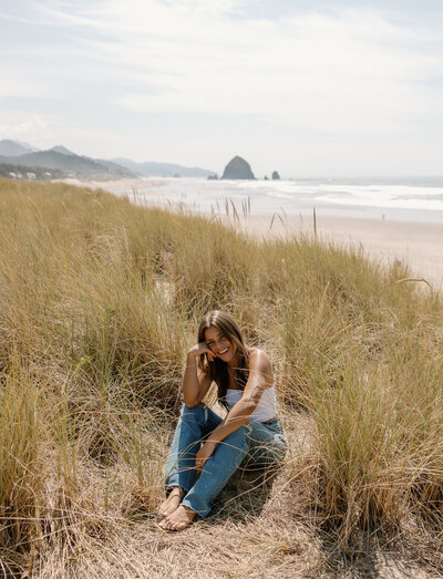 Portrait of photographer sitting in the coastal grass dunes at Cannon Beach with Haystack Rock in the distance.