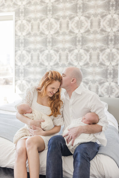 Husband kissing his wife's head while holding newborn twins -Newborn Photographer Greenville