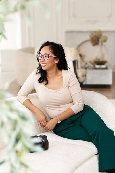 Portrait of Anh Nguyen, photographer behind Anh Point Photography, smiling off to the side while sitting on the couch.