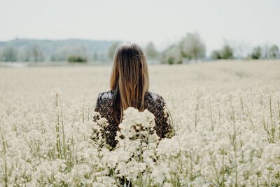 The back of a woman surrounded by wildflowers, evoking a sense of tranquility, connection to nature, and holistic wellness.